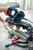 A person adjusts a mitre saw with a circular blade on a workbench.