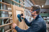 Person wearing safety equipment sanding a wooden cabinet door with a random orbit sander.