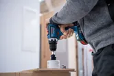 A person drills a hole in wood with a cordless power drill.