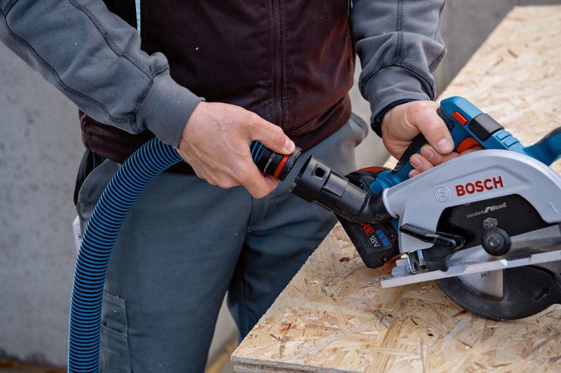 Person connects a dust extraction hose to a circular saw on a wooden workbench.
