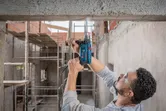 A person wearing safety equipment drills into a concrete beam at a construction site.
