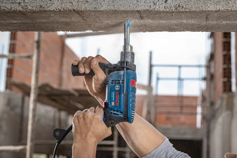 A person drills into a concrete ceiling with an impact drill at a construction site.