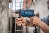 A person drills into concrete with an impact drill at a construction site.