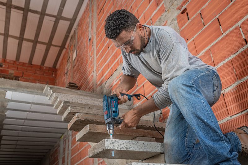 A person wearing safety equipment drills into a concrete staircase with an impact drill.