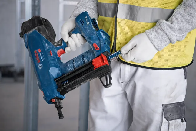 A person wearing safety equipment loads nails into a cordless nail gun.