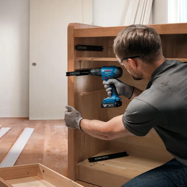 Person wearing safety equipment installs drawer slides using a cordless drill.