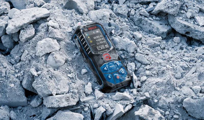 Laser measure device resting on broken concrete debris outdoors.