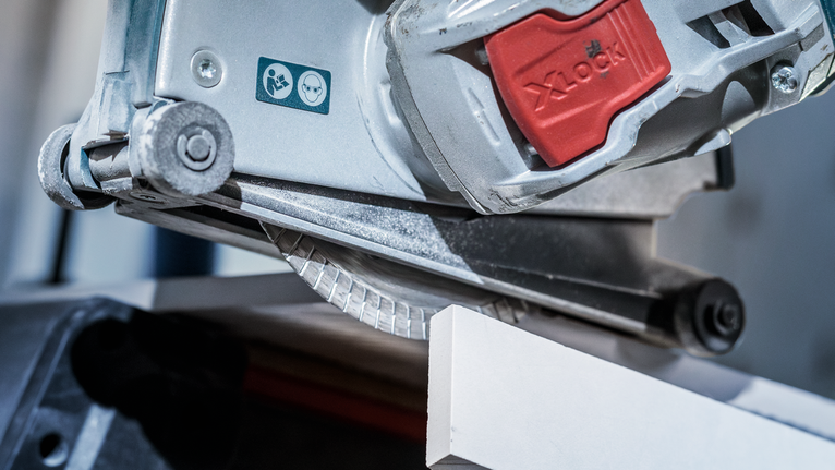 Circular saw cutting a white tile with a safety warning label visible.
