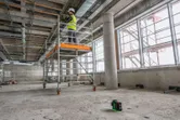 A person wearing safety equipment works on scaffolding, with a laser leveling tool projecting lines.