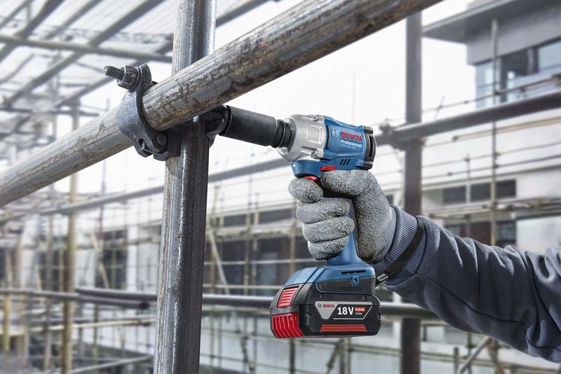 A person wearing safety equipment uses a cordless impact wrench on scaffolding.