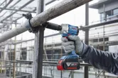 A person wearing safety equipment uses a cordless impact wrench on scaffolding.