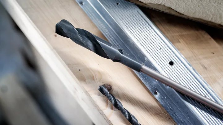 Large and small drill bits placed on a wooden surface near a metal guide.