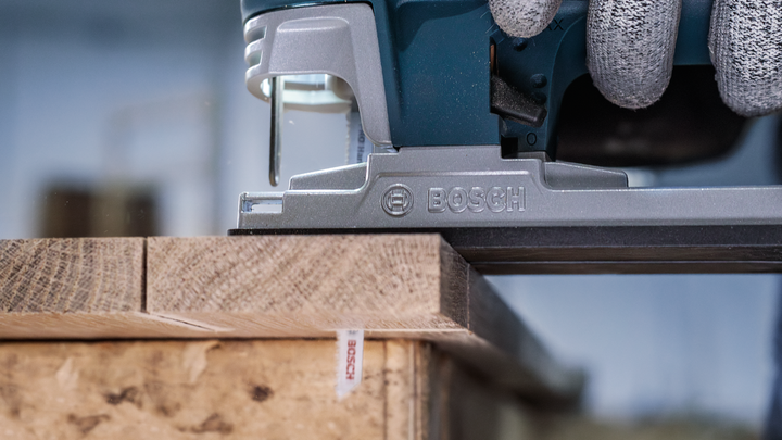 Person wearing safety equipment uses a jigsaw to cut a wooden board.