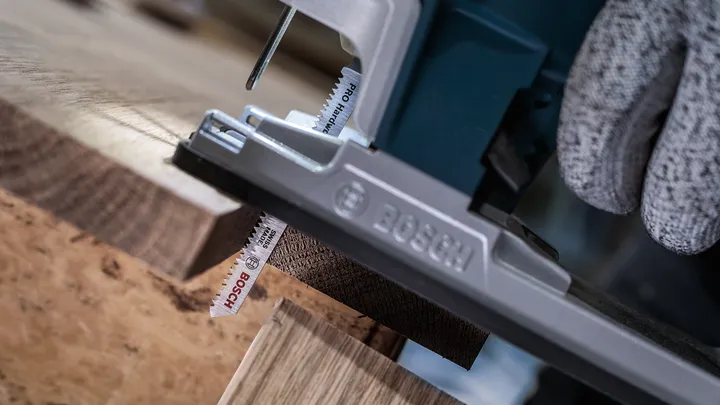 Person wearing safety equipment uses a jigsaw to cut a wooden board.