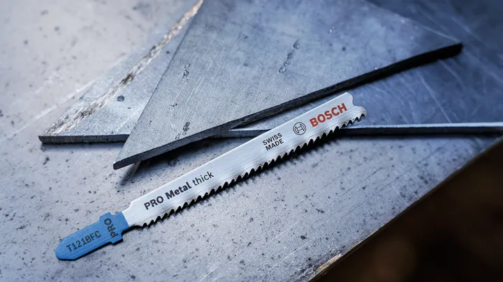 Metal saw blade resting on a steel surface next to cut metal sheets.