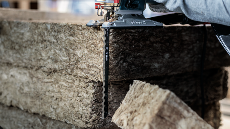 Person using a jigsaw to cut through thick insulation material.