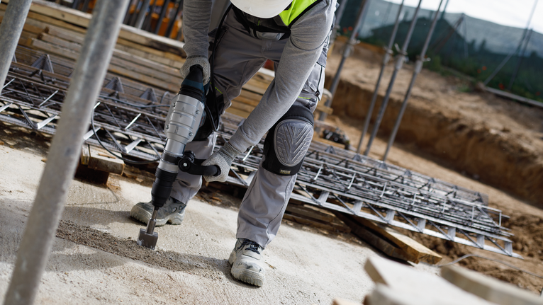Person wearing safety equipment uses a demolition hammer on a construction site.