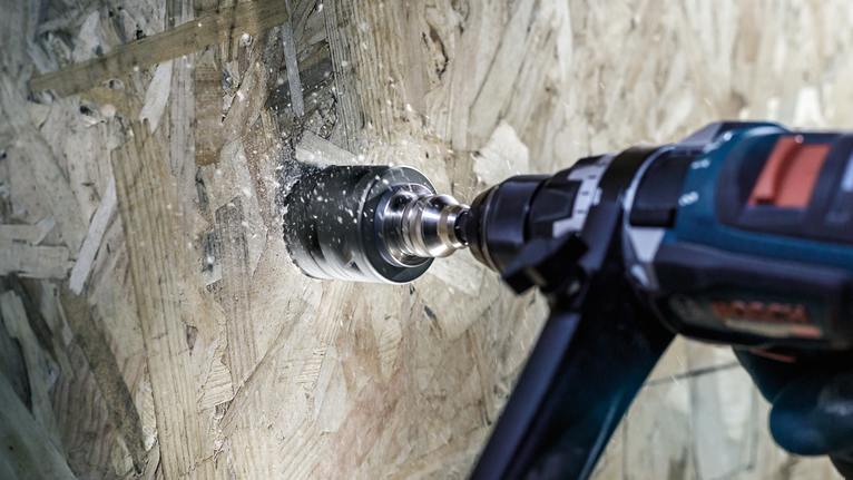 Power drill with hole saw attachment cutting through a wooden board.
