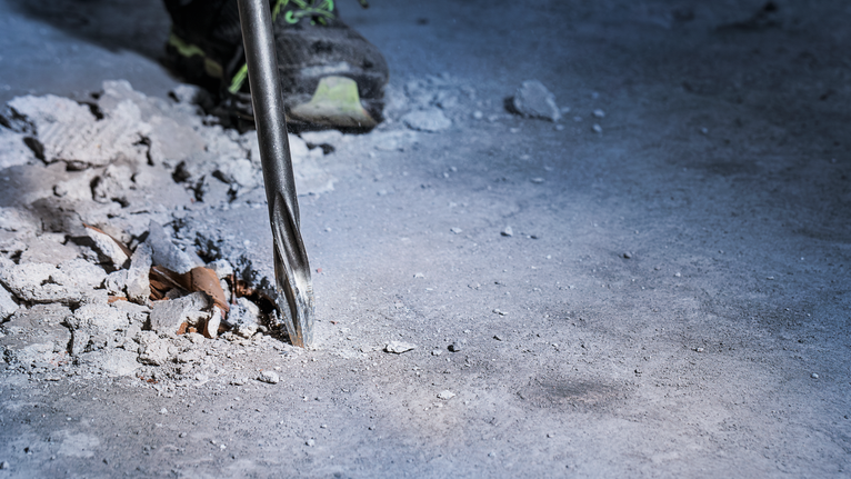 Drill bit breaking concrete on a construction site.
