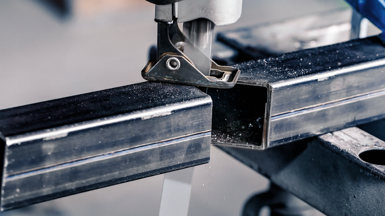 Jigsaw cutting through a metal rectangular tube on a workbench.