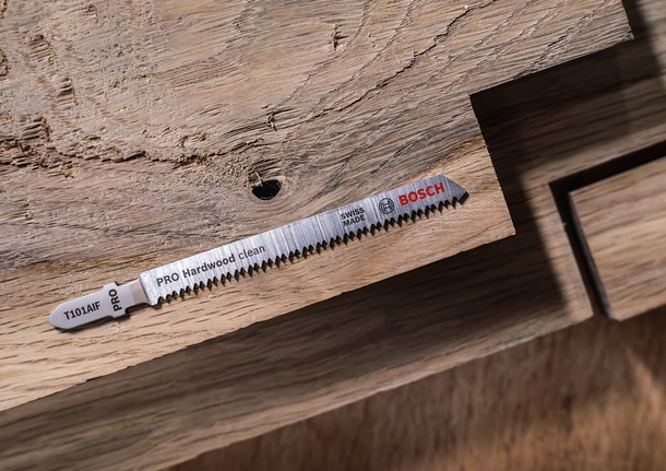 Jigsaw blade placed on a wooden surface with a cutout section.