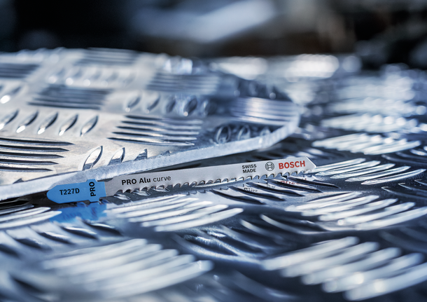 Metal jigsaw blade resting on textured aluminum sheet.