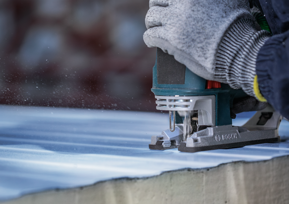 Person wearing safety equipment cutting a stone slab with a jigsaw.