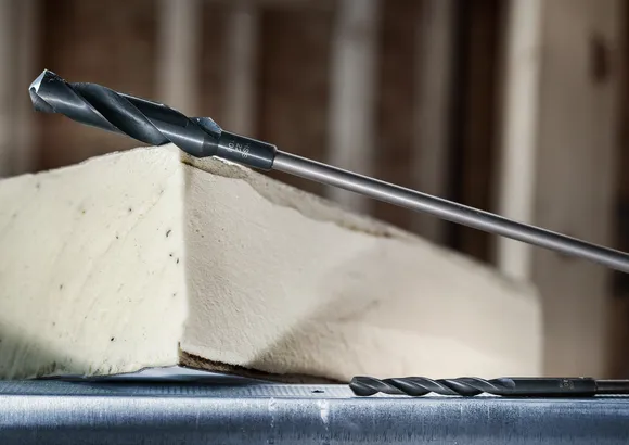 Two drill bits positioned near a block of foam insulation.