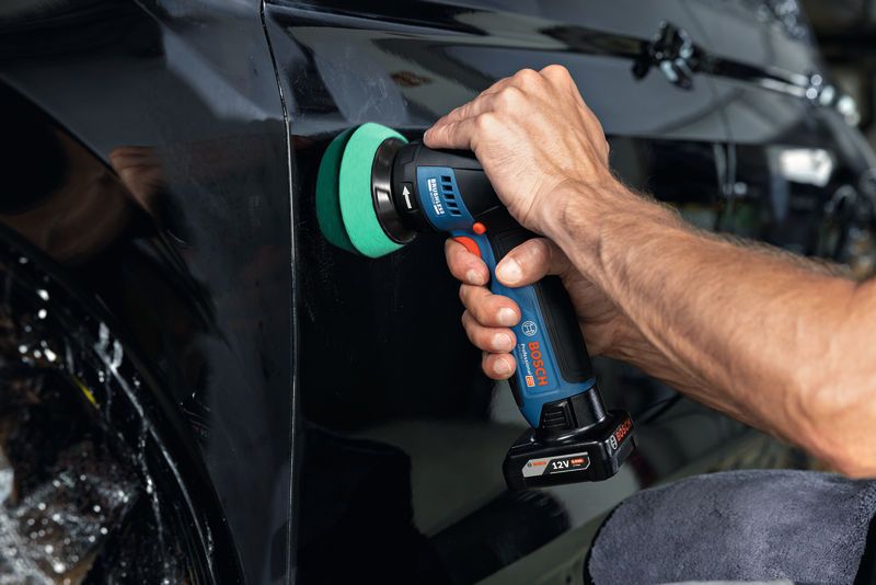 A person uses a cordless polisher to buff the surface of a black car door.