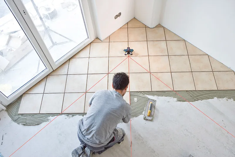 A person aligns floor tiles using a tile laser leveling tool.