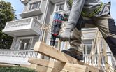 A person wearing safety equipment drills into stacked wooden beams at a construction site.