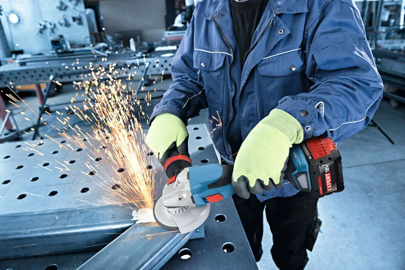 A person wearing safety equipment grinds metal with a cordless angle grinder.