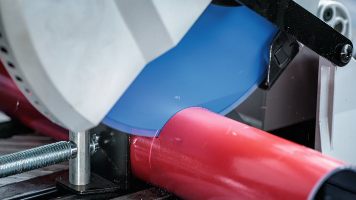 Metal-cutting saw slices through a red pipe secured in a clamp.