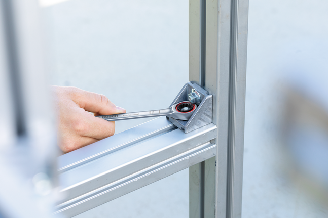 Person uses a ratcheting wrench to tighten a bolt on a metal frame joint.