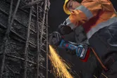 A person wearing safety equipment uses an angle grinder to cut steel rebar.