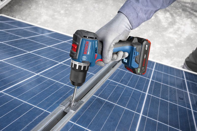 A person wearing safety equipment uses a cordless drill on a solar panel frame.