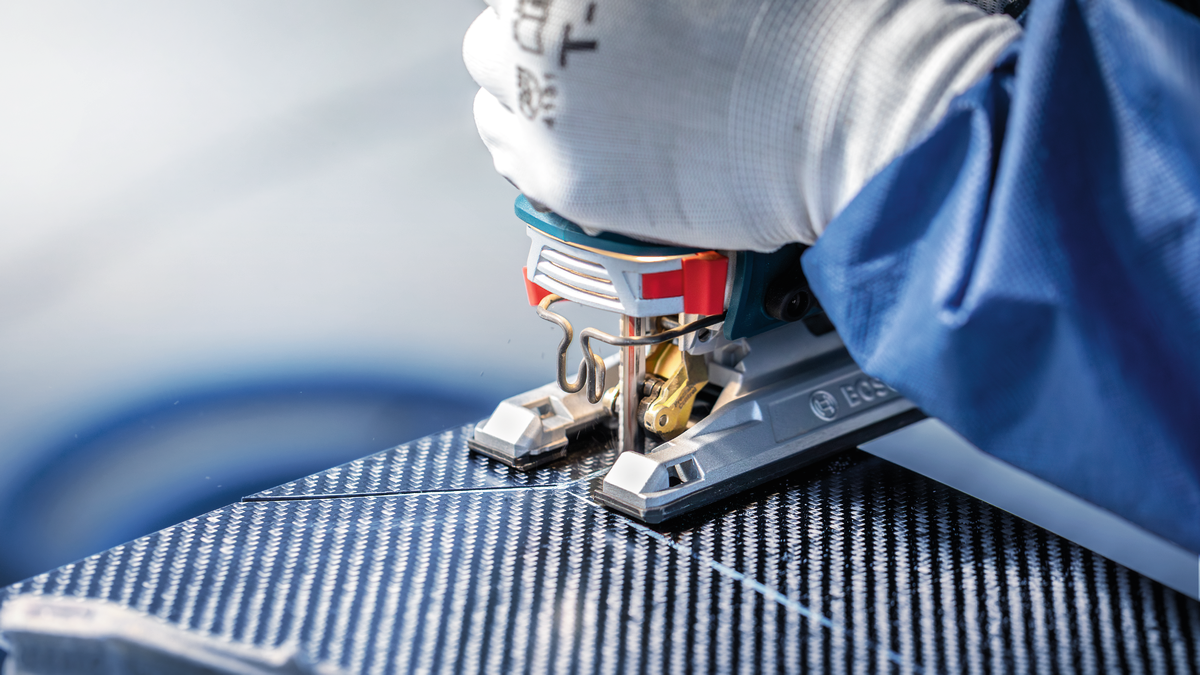 Person wearing safety equipment cuts a patterned panel with a jigsaw.