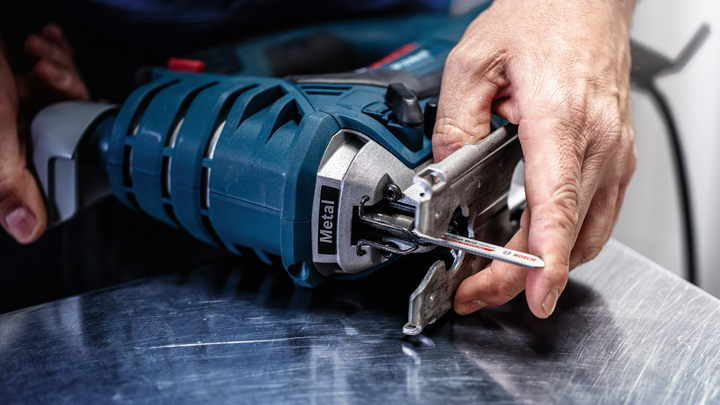 Person attaches a jigsaw blade to a power tool on a metal surface.