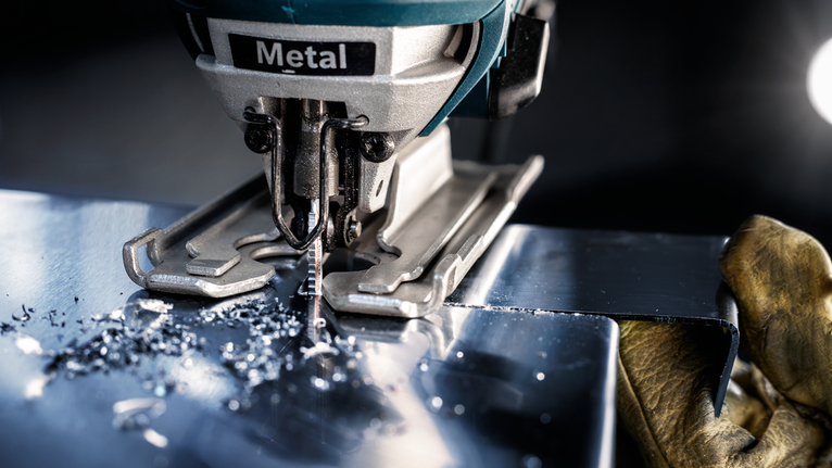 Person wearing safety equipment uses a jigsaw to cut a sheet of metal.
