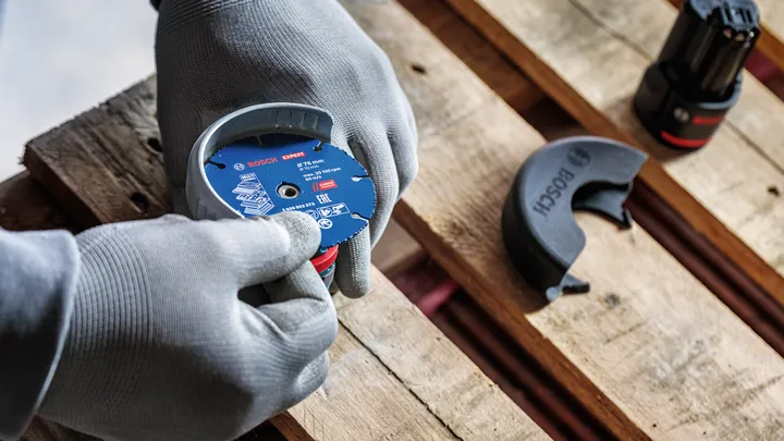 Person wearing safety equipment attaches a grinding disc on a wooden pallet.
