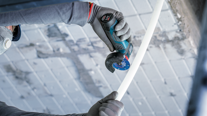 Person wearing safety equipment cuts a white pipe with a rotary tool.