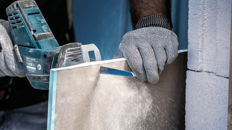 Person wearing safety equipment cuts a tile board using a power saw.