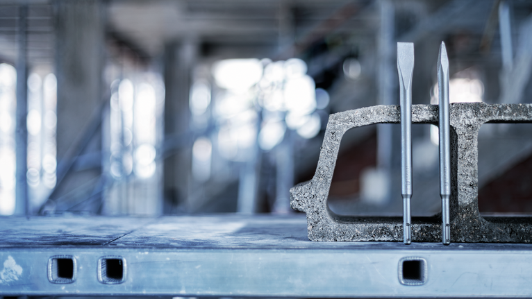 Two pointed chisels placed vertically inside a concrete block on a metal workbench.