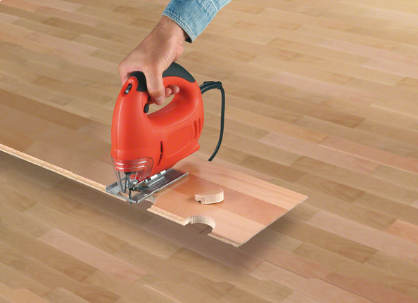 Una sierra caladora cortando una muesca curva en una tabla de piso laminado.