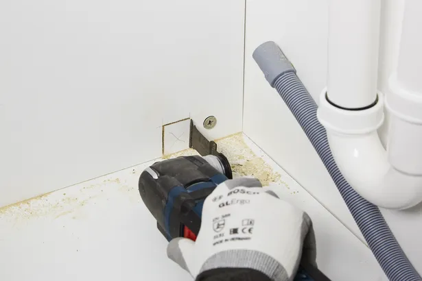 Un trabajador que usa equipo de seguridad corta una abertura cuadrada en un gabinete con una herramienta eléctrica.