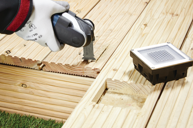 Un trabajador que usa equipo de seguridad corta una ranura en una plataforma de madera usando una herramienta multiusos.