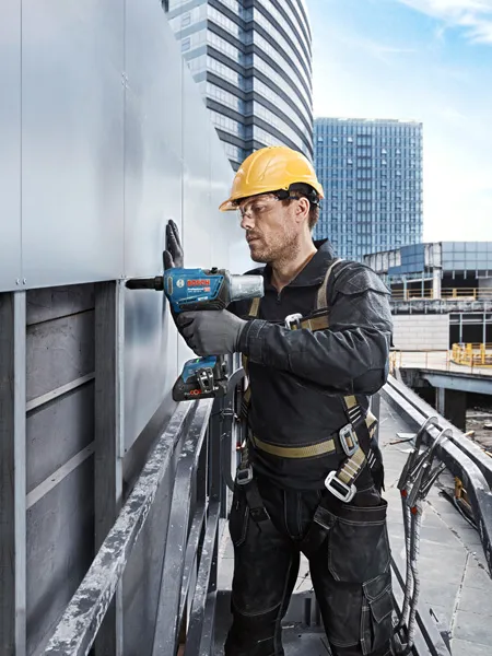 Una persona que usa equipo de seguridad perfora un panel metálico en el exterior de un edificio.