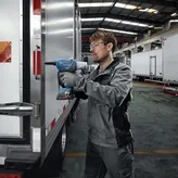 Una persona que usa equipo de seguridad utiliza una llave de impacto inalámbrica en la puerta de un camión.