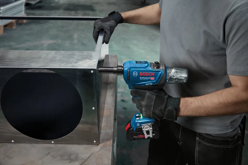 Una persona que usa equipo de seguridad utiliza una llave de impacto inalámbrica en un conducto de metal.