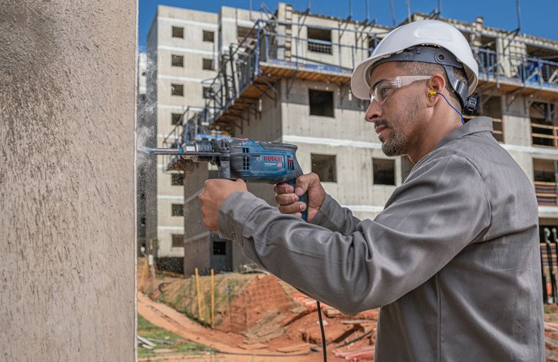Una persona que usa equipo de seguridad perfora una pared de hormigón en un sitio de construcción.
